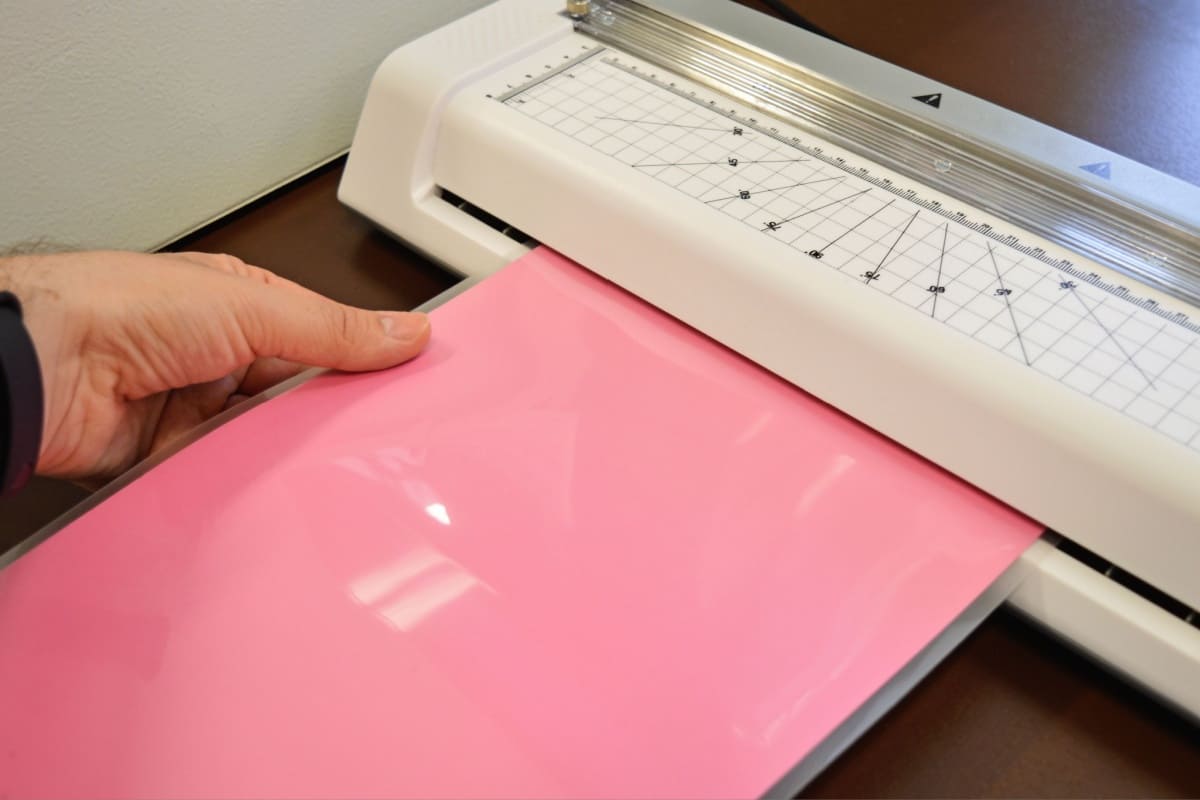 laminator laminand o hartie roz, un om tine mana pe hartia laminata