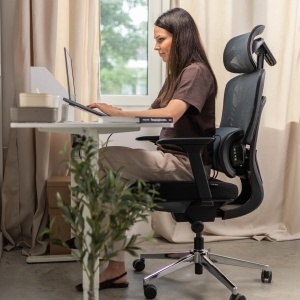 Žena sedi za radnim stolom na Mark Adler Visioner 6.1 Black ergonomskoj stolici sa ugrađenim masažerom